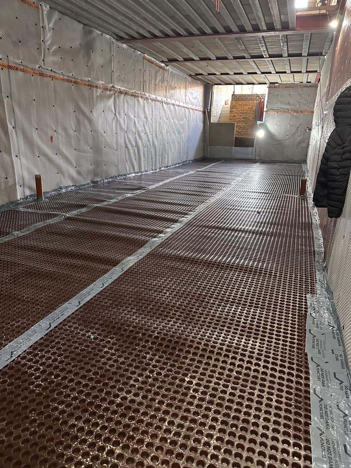 Long basement lined with drained cavity membrane on the walls and floor, with the new stair at the far end