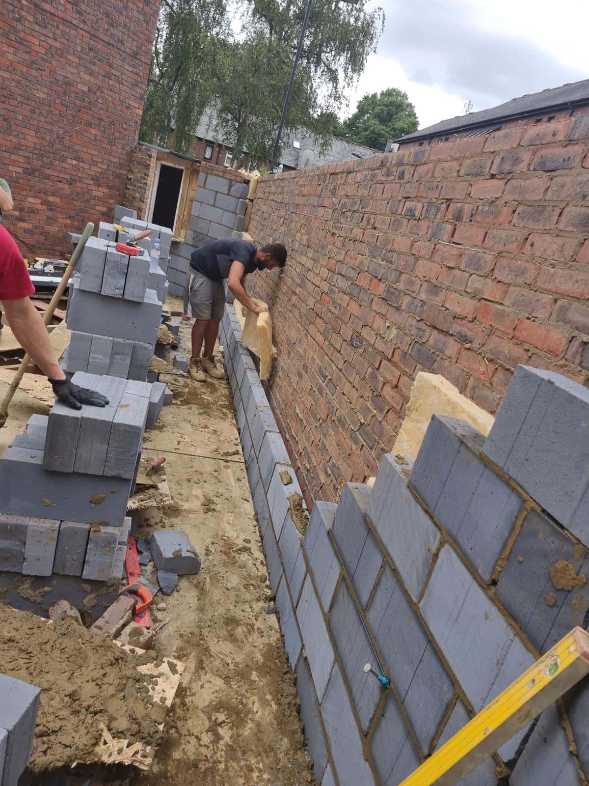 Bricklayers raising the blockwork of a new house between existing brick walls