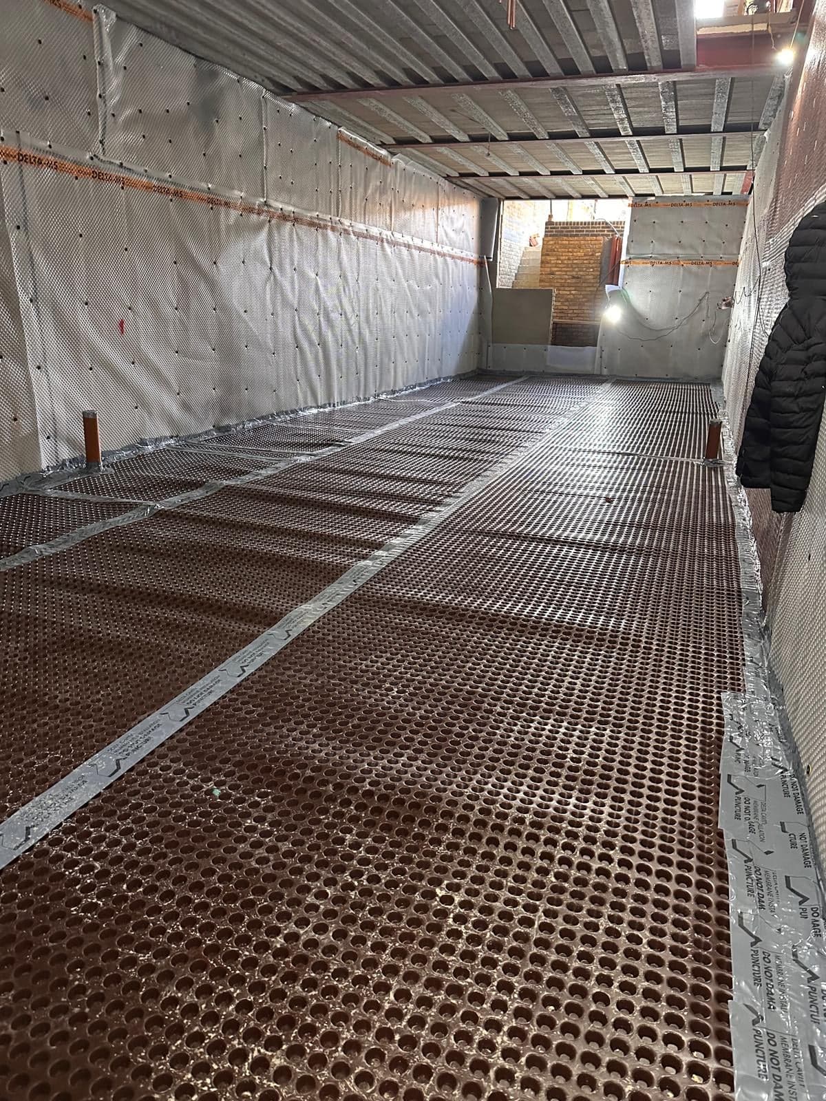 Long basement lined with drained cavity membrane on the walls and floor, with the new stair at the far end