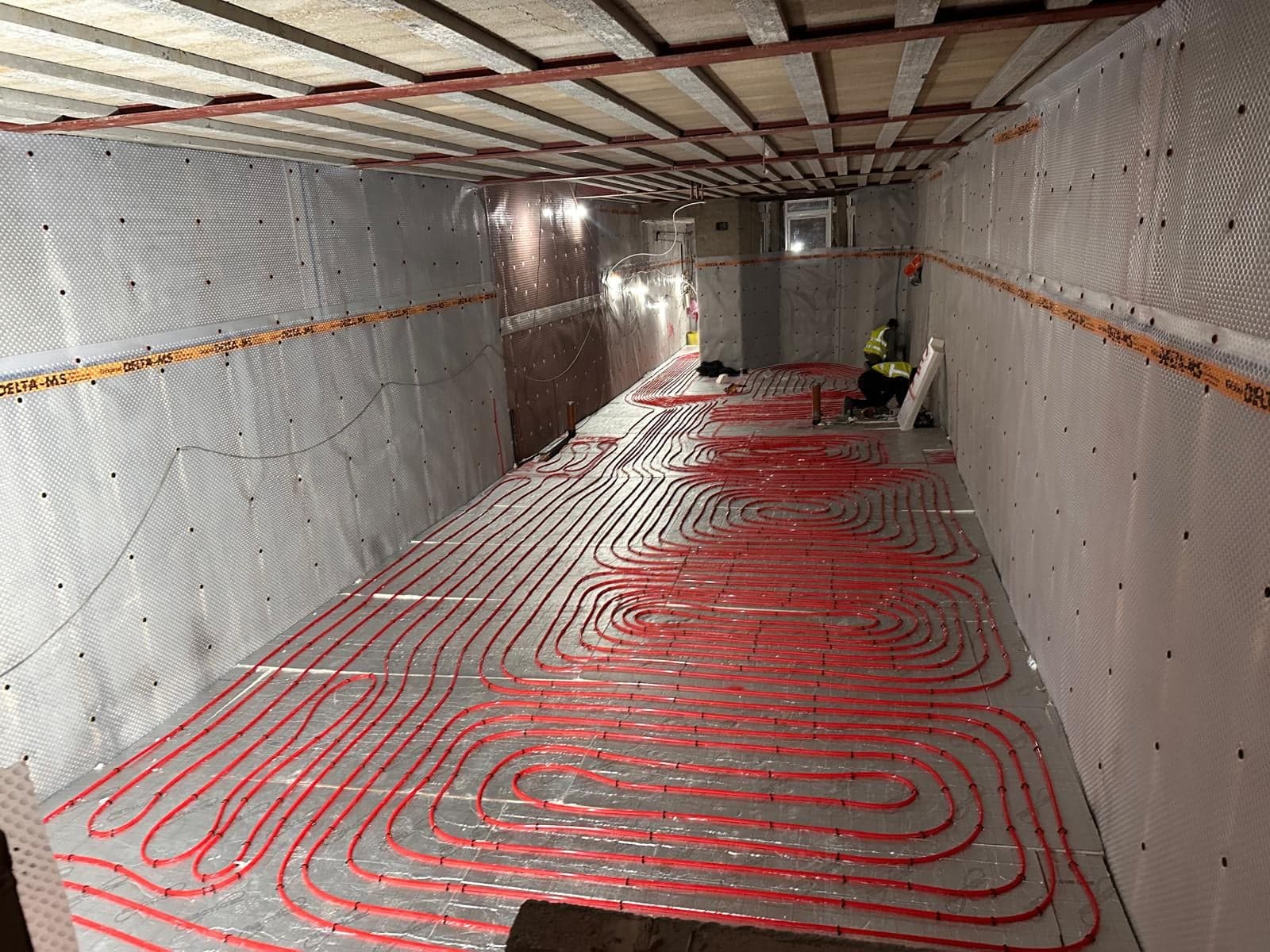 Underfloor heating pipes laid across a new basement, with the walls lined in cavity drain membrane