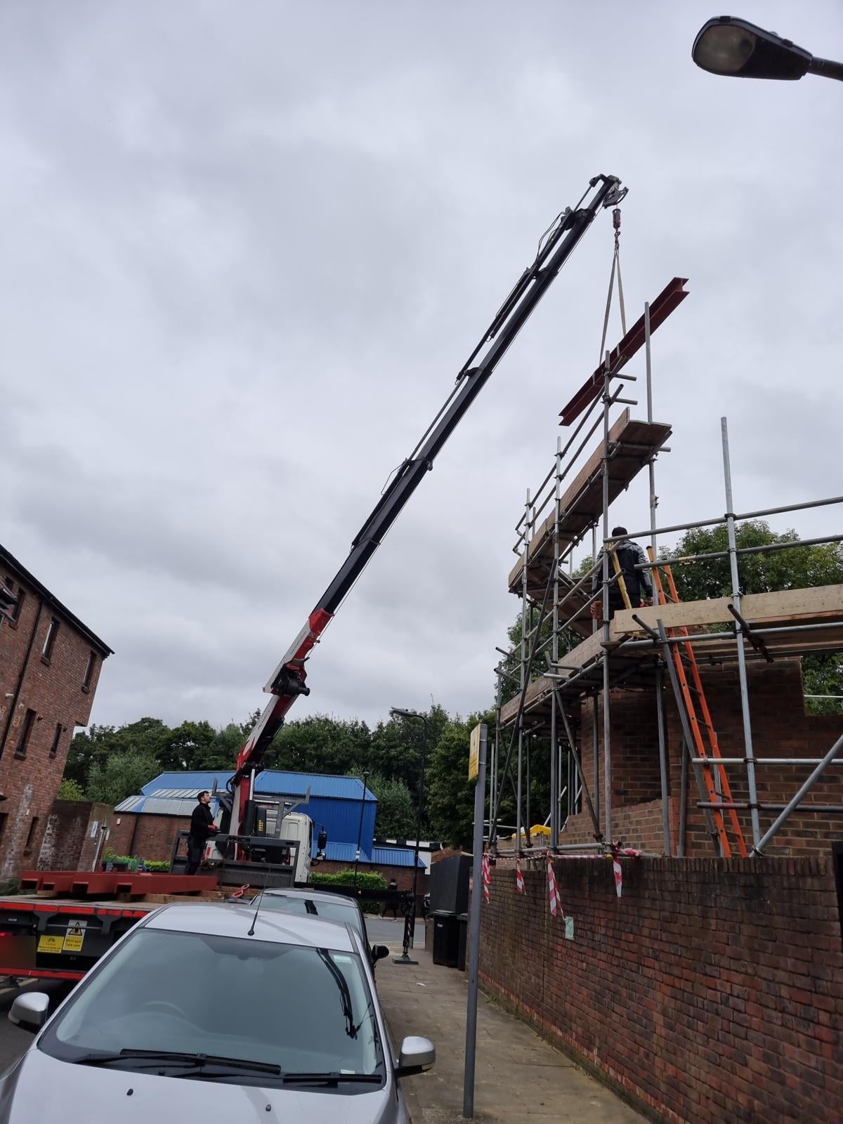Lorry crane lifting a steel beam up to the scaffold